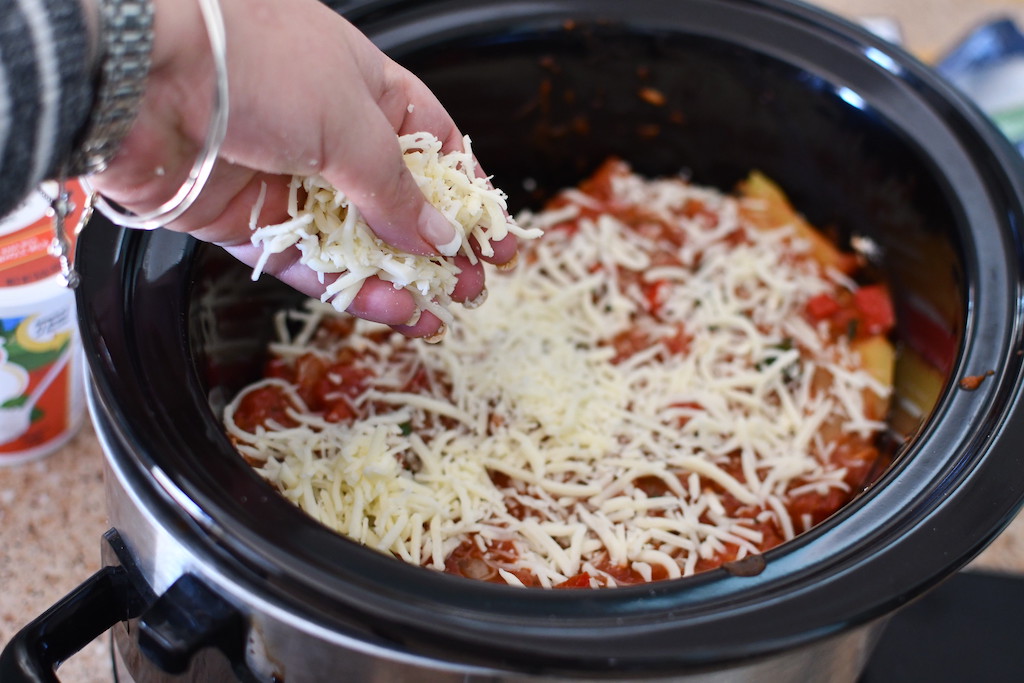 sprinkling shredded cheese on top of veggie lasagna in slow cooker