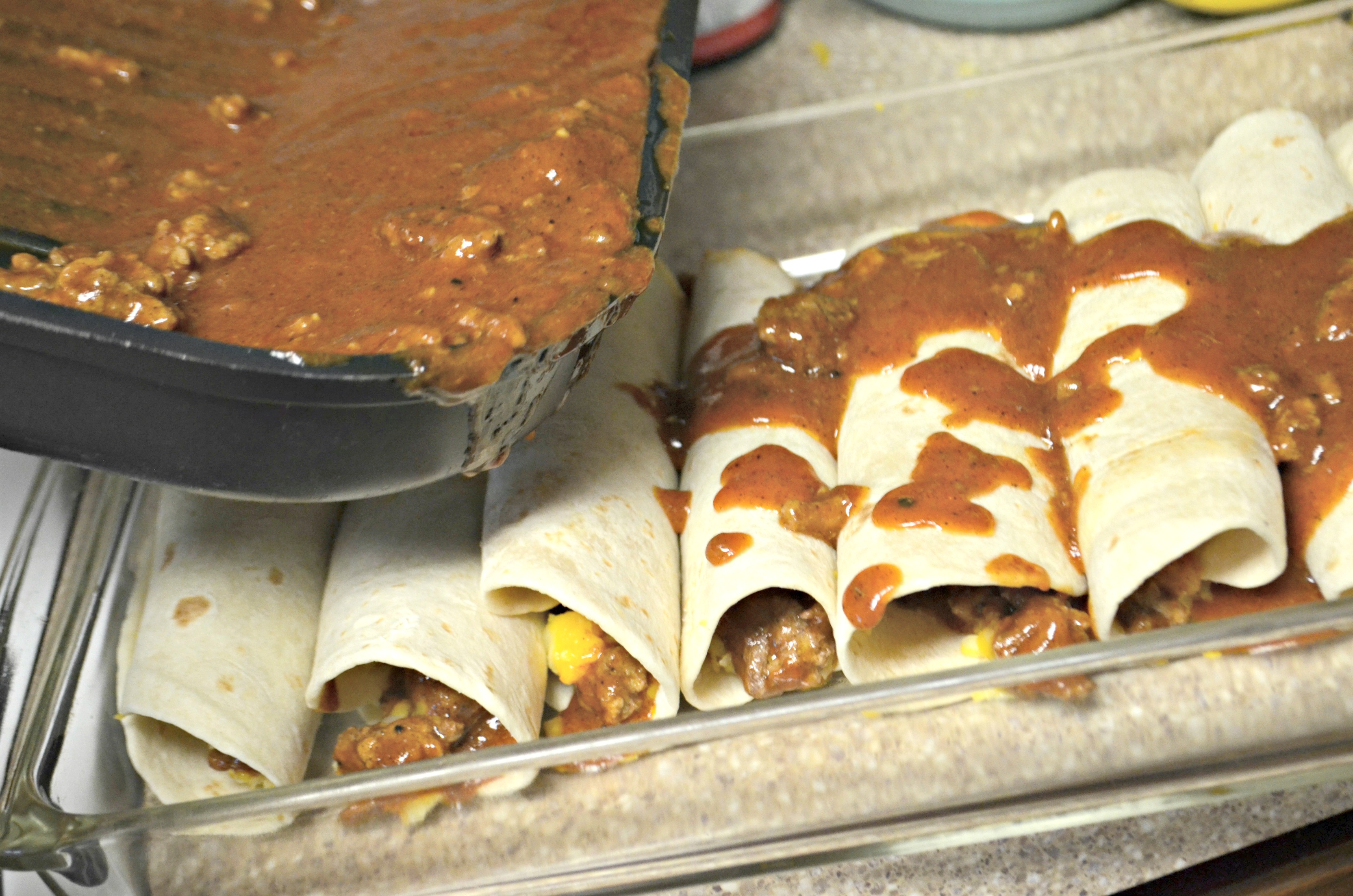 pouring enchilada sauce over the enchiladas in the pan