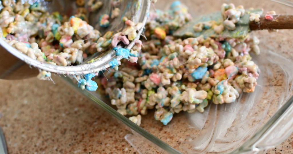 pouring in lucky charms marshmallow treats into pan