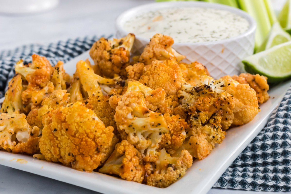 Buffalo Cauliflower Bites on a plate with ranch and sliced limes