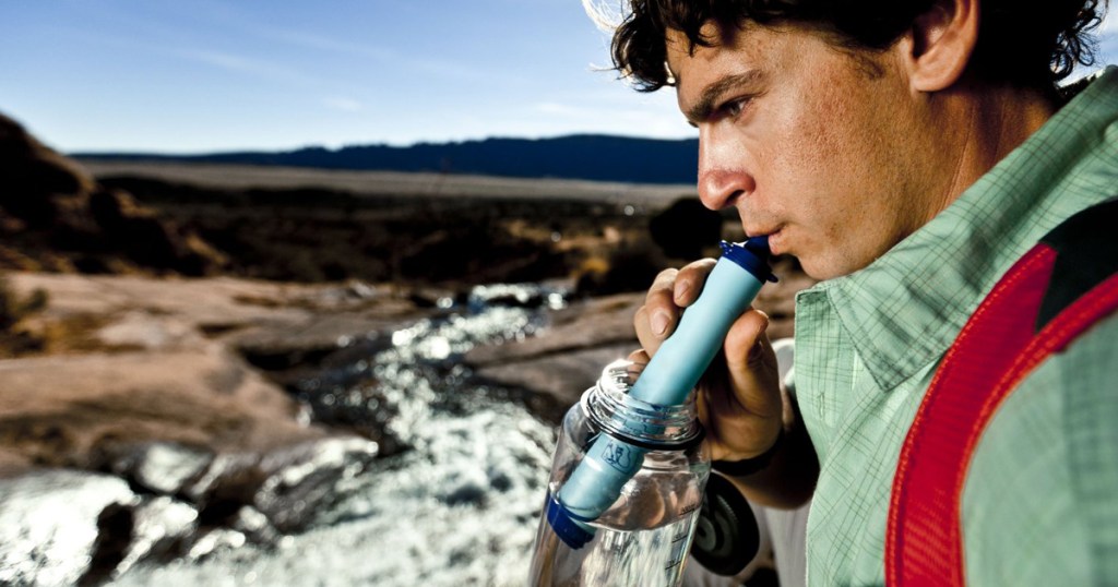 man using lifestraw in jar of water