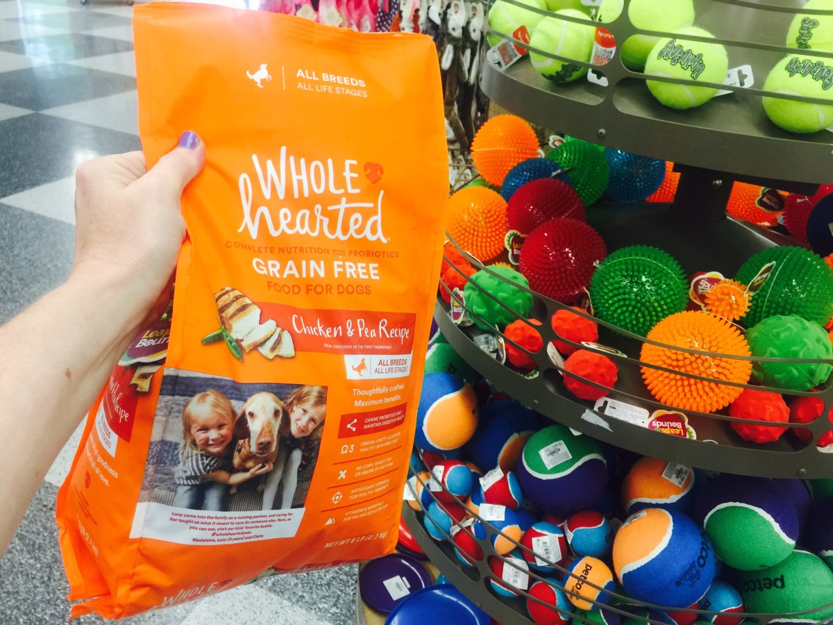 hand holding up a bag of whole hearted dog food in front of a display of dog toys