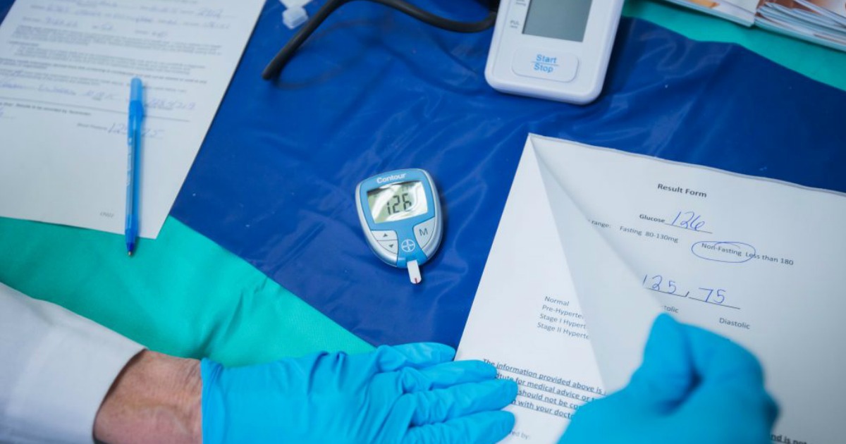 pair of gloved hands reading paperwork with a glucose tester next to them