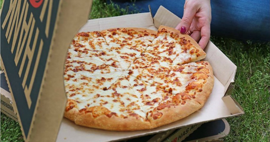 Hand pulling piece of cheese pizza out of cardboard pizza box