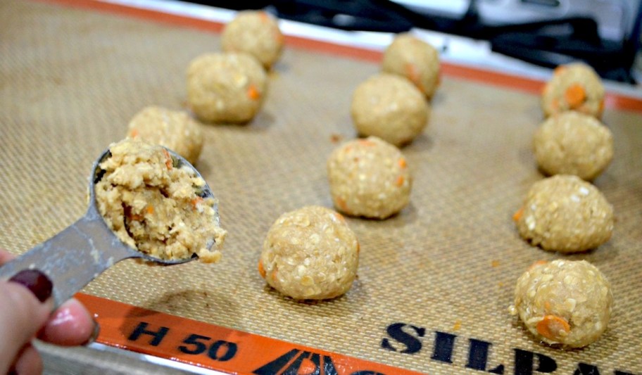 hand scooping measuring spoonful of salted caramel oatmeal cookie batter onto baking sheet