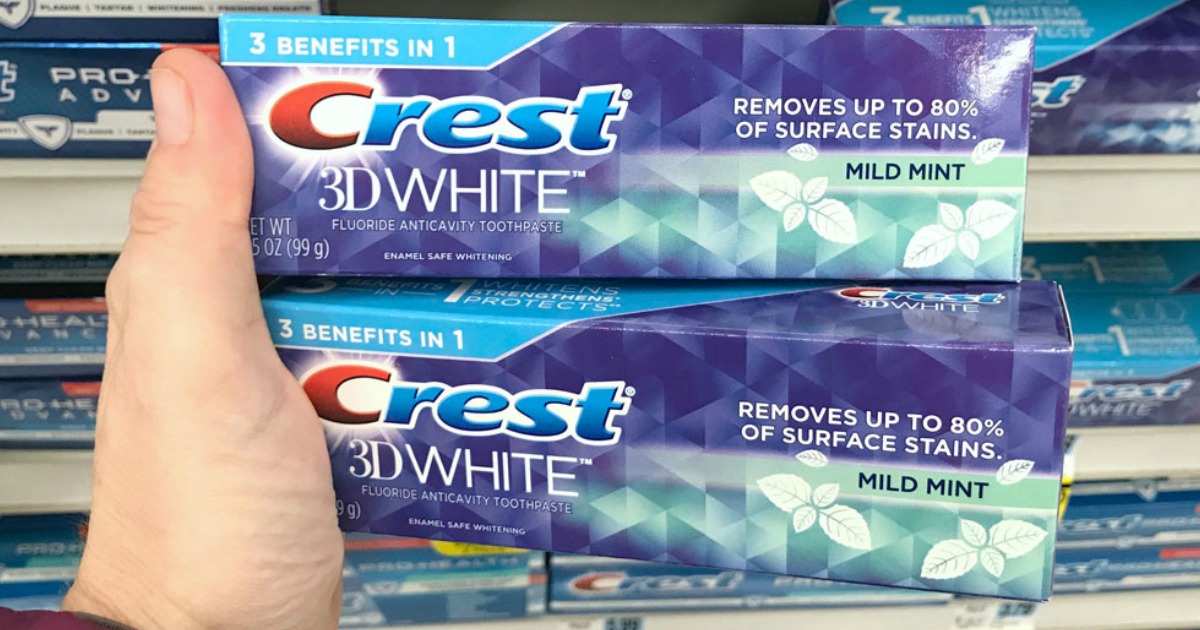 hand holding two boxes of Crest 3D White toothpaste in front of store shelf