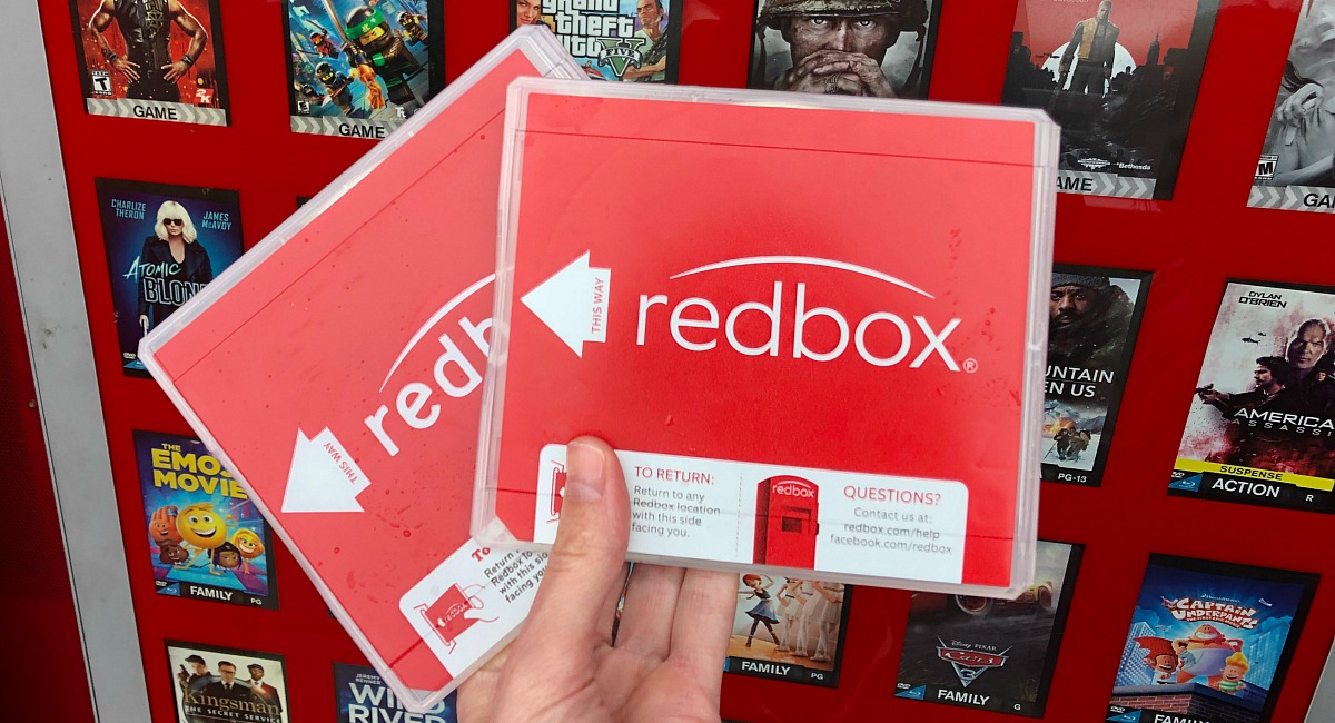 a hand holding two Redbox movie cases outside of the Redbox kiosk