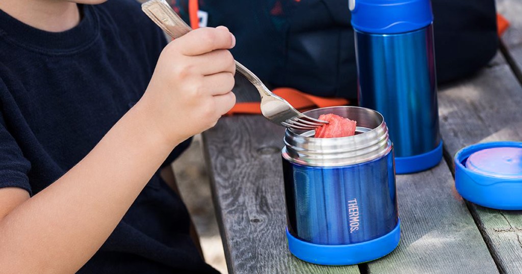 child using a fork to eat fruit out of a stainless steel food jar