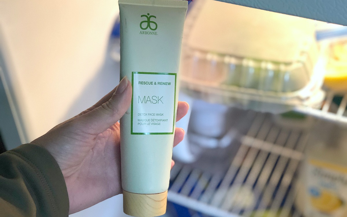 hand holding green bottle of face mask in front of fridge