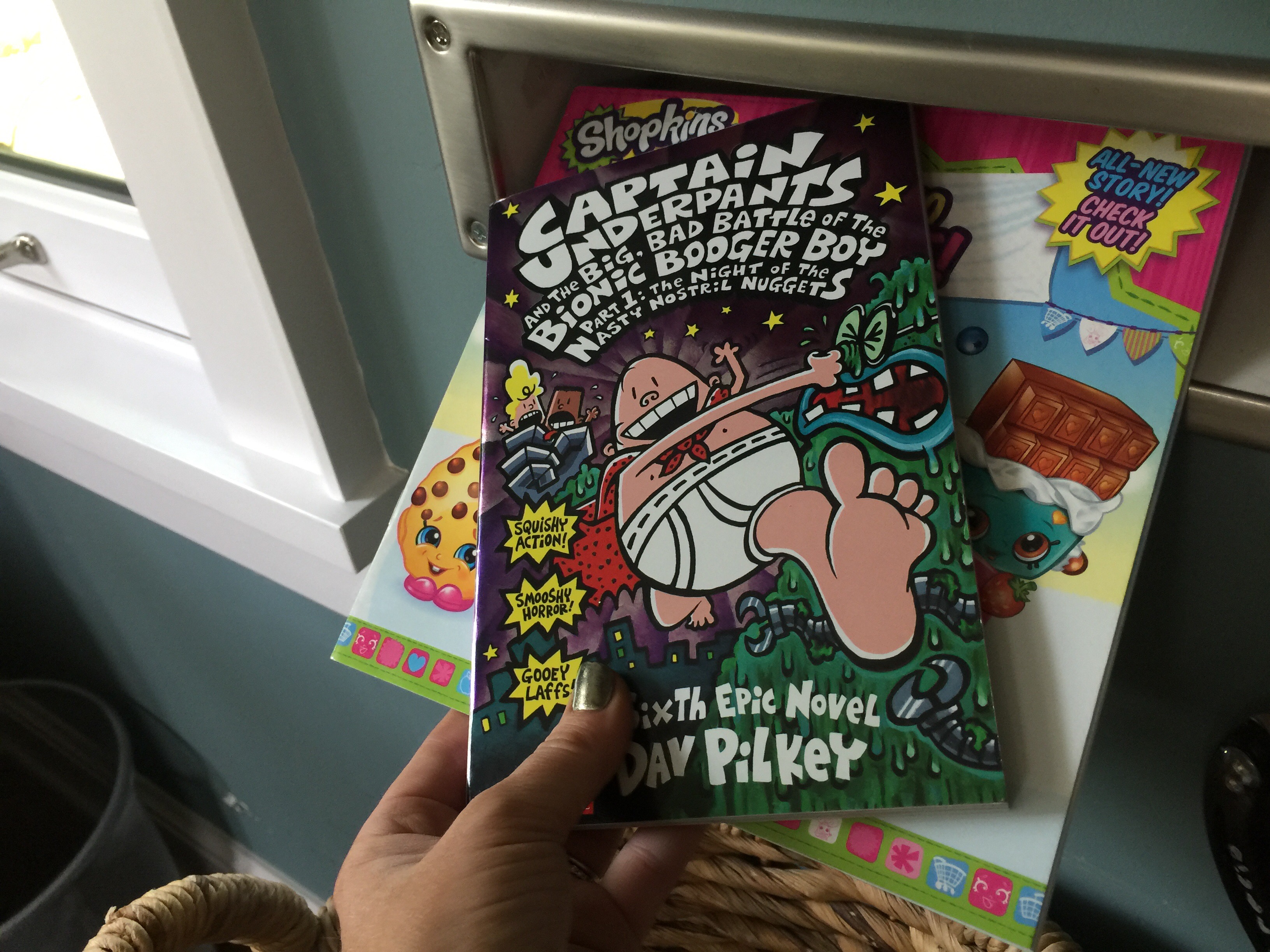 hand holding a Captain Underpants and Shopkins book