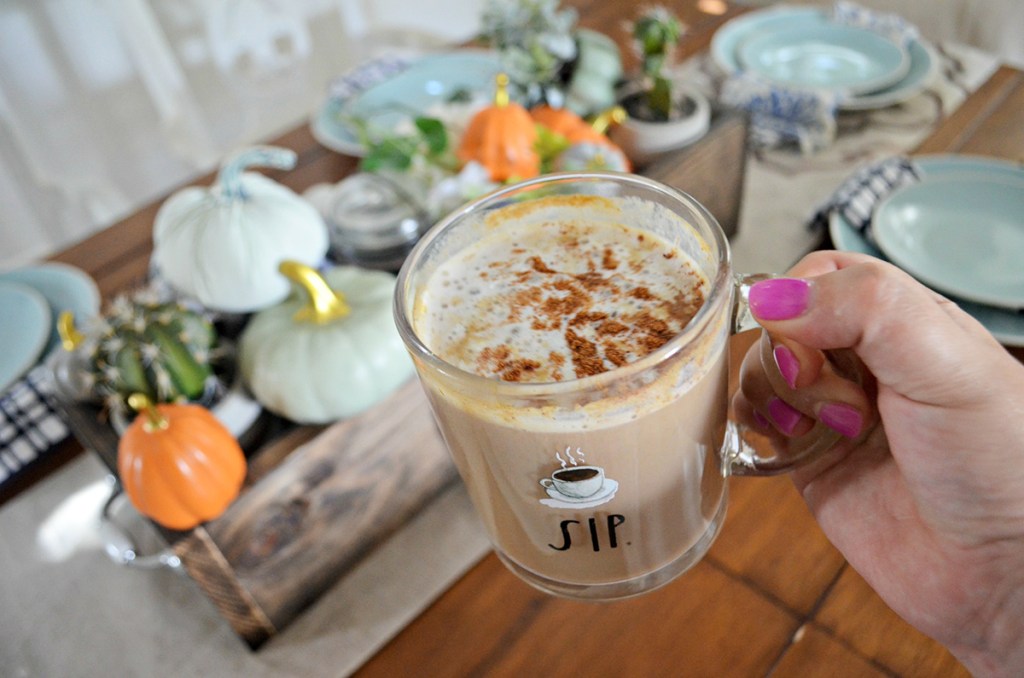 hand holding pumpkin spice latte in front of tablescape