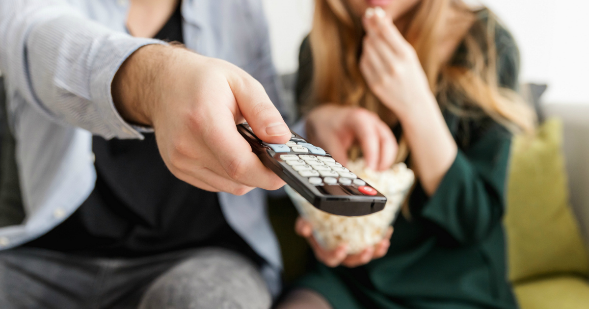 Man and woman watching television, with man holding the remote