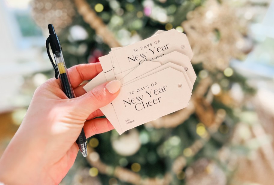 hand holding 30 days of new year cheer gift tags in front of christmas tree