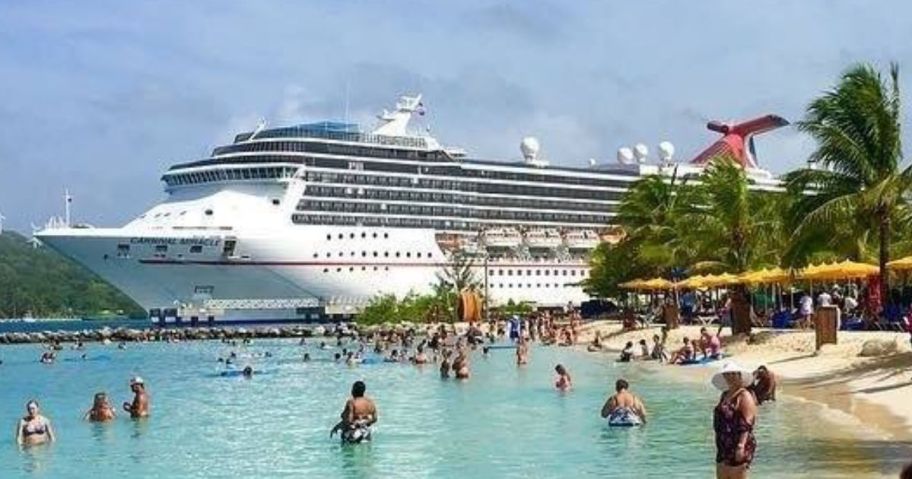 Carnival Cruise ship docked at a distance beach and ocean with people in front of it