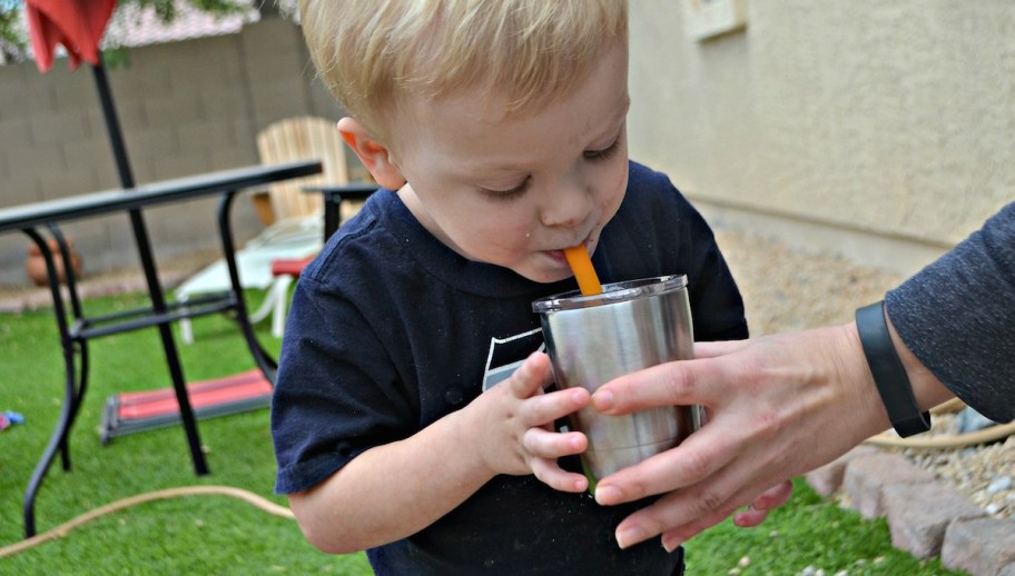 boy drinking water outside with parent holding stainless steel mug cup