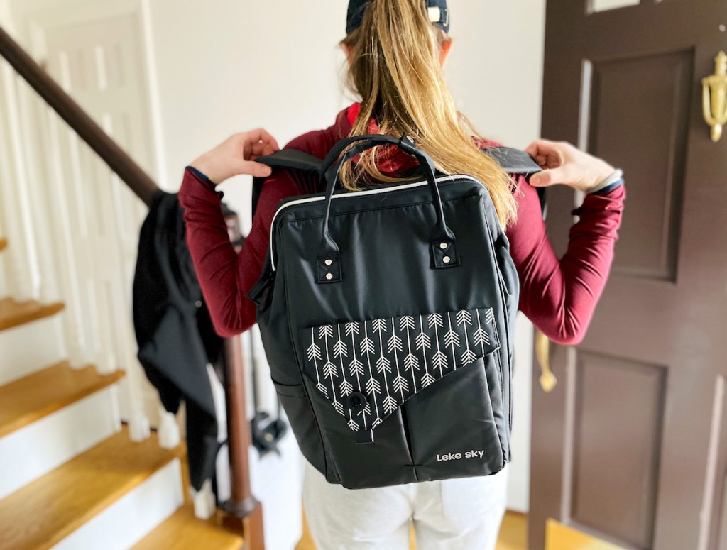 woman putting on black travel backpack in front of doorway and stairs