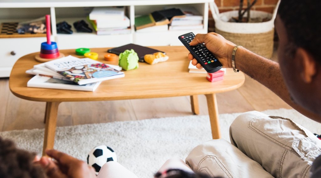 man holding a remote with coffee table in the background with magazines and messy toys 