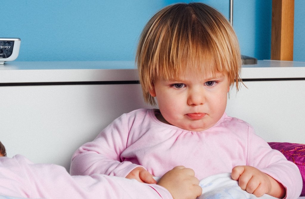 sad toddler girl sitting on bed wearing a pink shirt