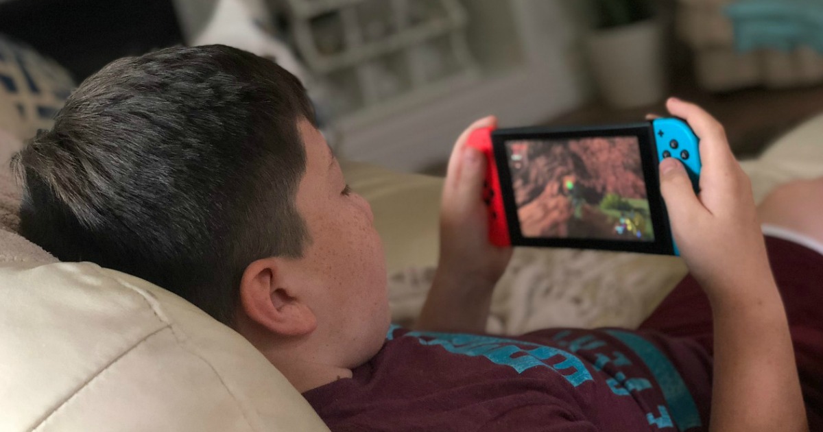 young boy playing nintendo switch while lounging on couch