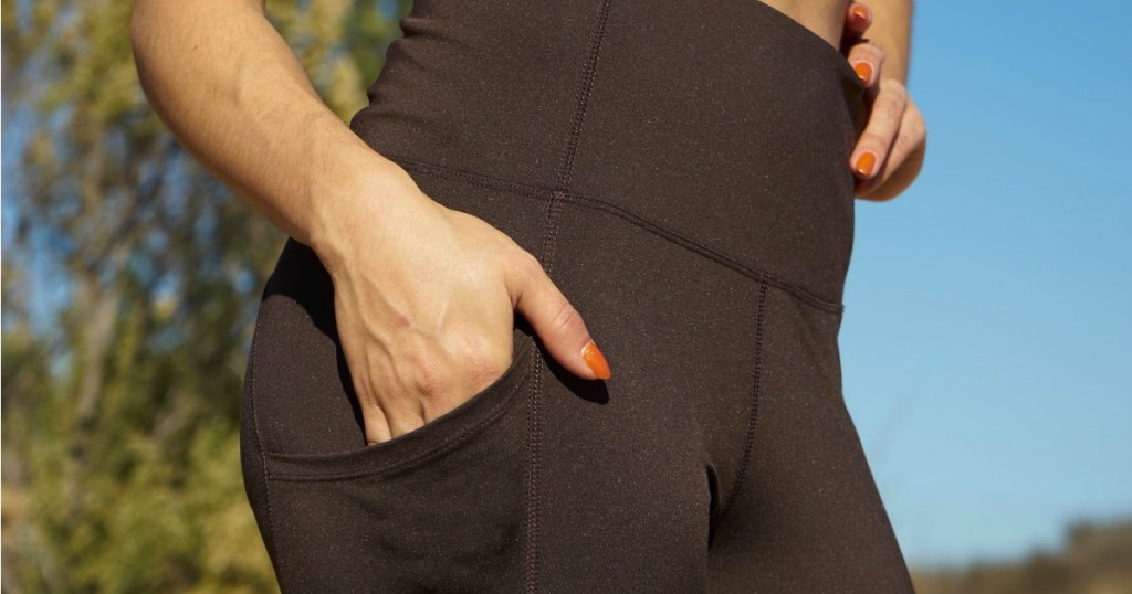 woman putting hand in pocket of black marika leggings outside