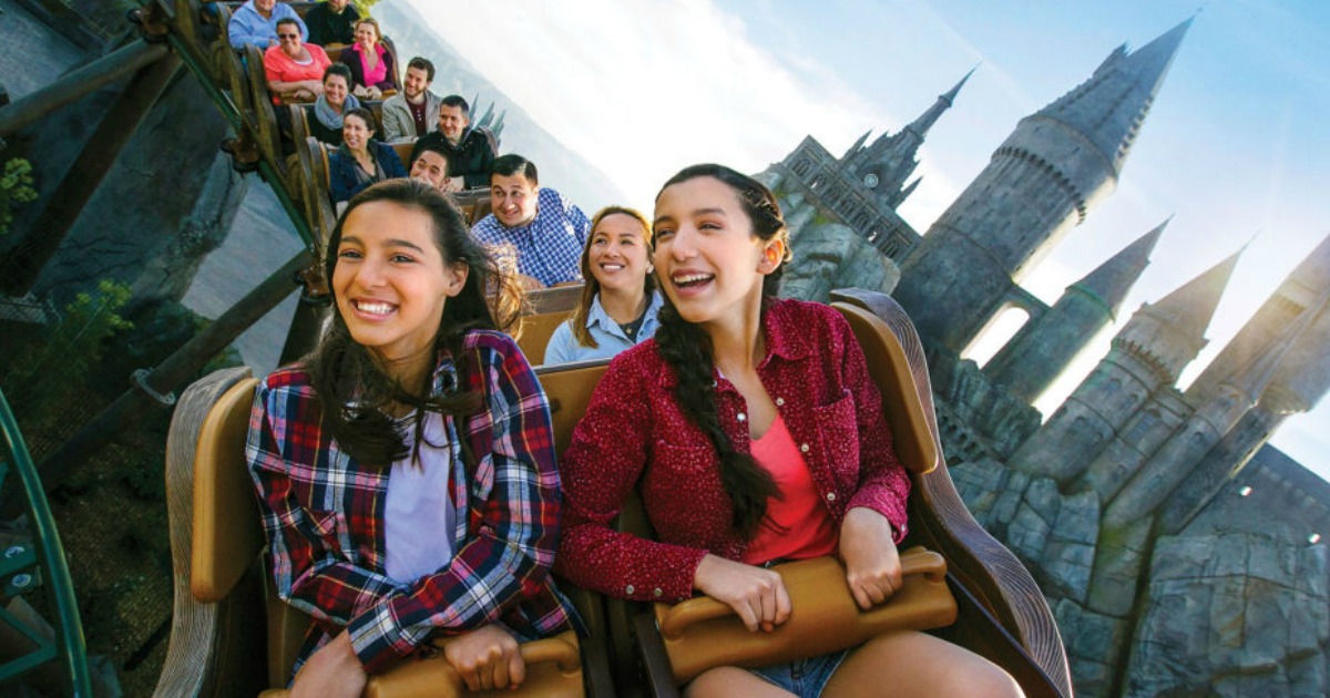 people riding roller coaster with castle in the background 