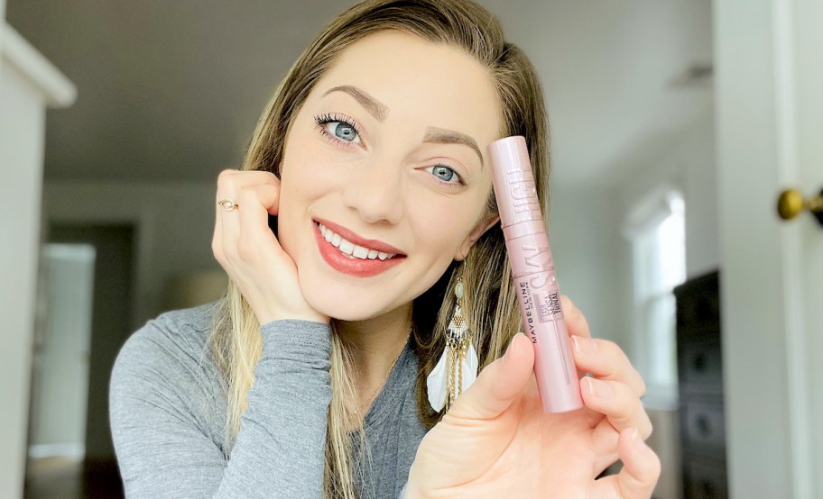 woman holding mascara in hand with one eye wearing mascara