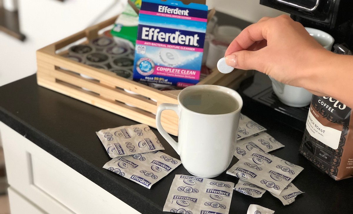 hand holding round tablet over water filled white mug with box and coffee in background