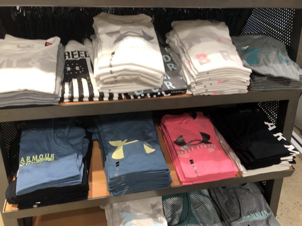 Under Armour Tees in various colors folded on a store display shelf