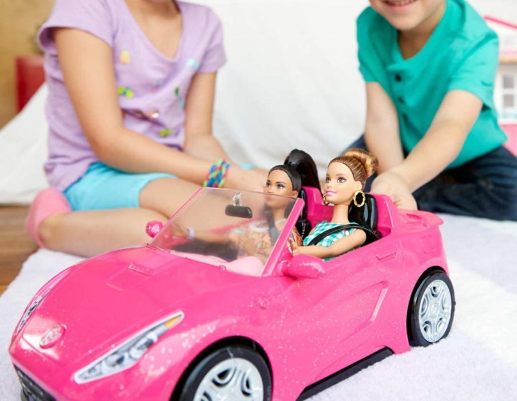 barbie convertible with two barbies in car and kids in background