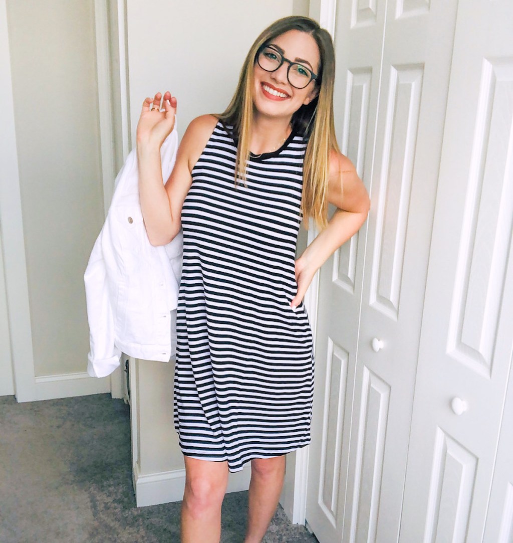 woman smiling holding white jean jacket wearing black white stripe dress