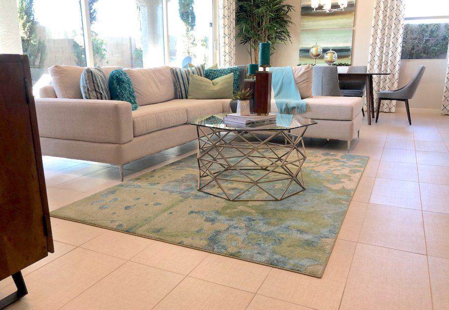 living room with blue and green rug beige sofa and glass coffee table