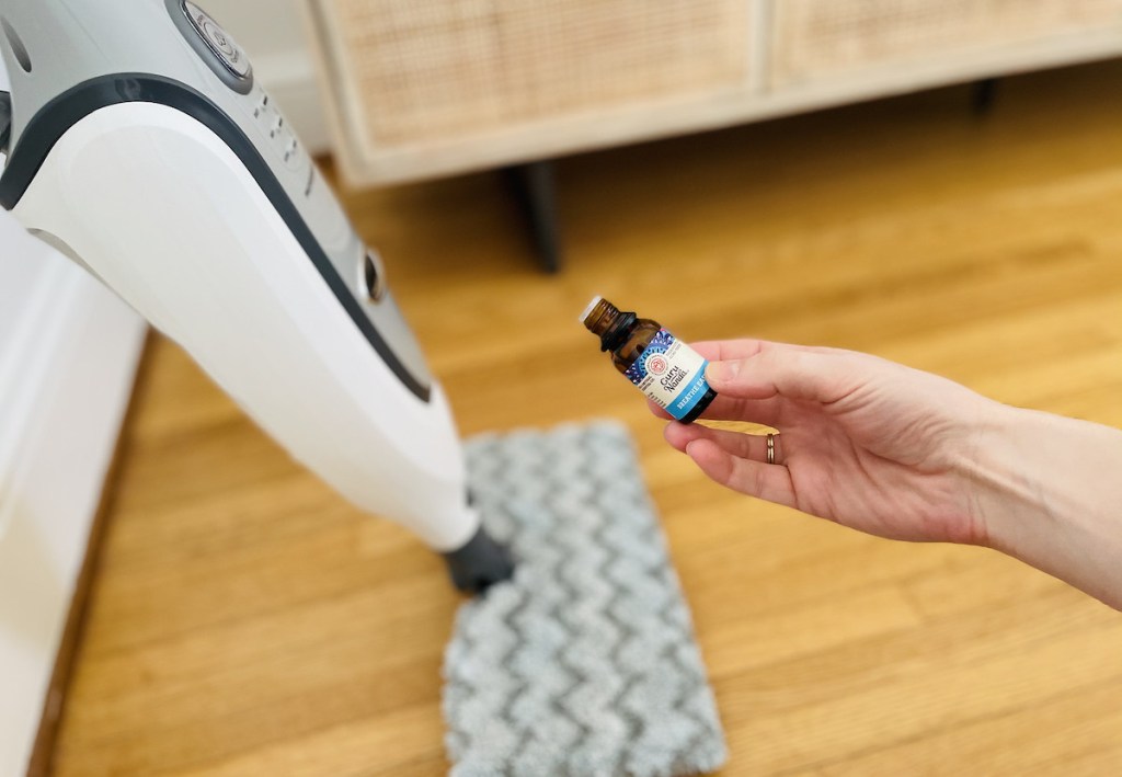 hand holding bottle of essential oils next to steam mop