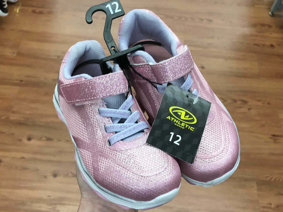 pair of pink glittery girls sneakers being held in a store