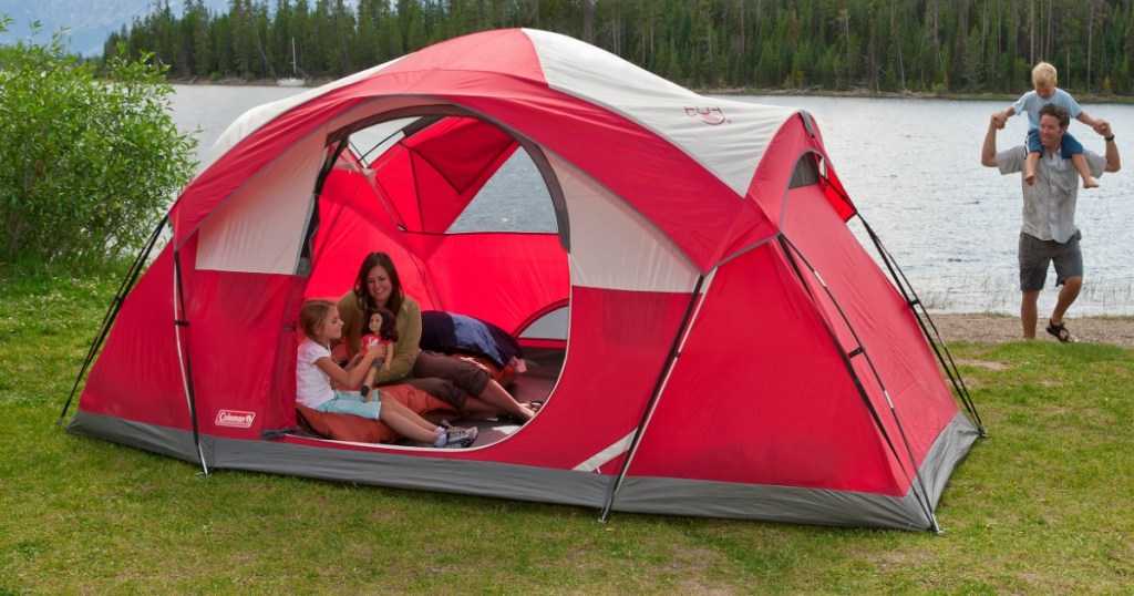 red tent with a family sitting in it and a lake in the background