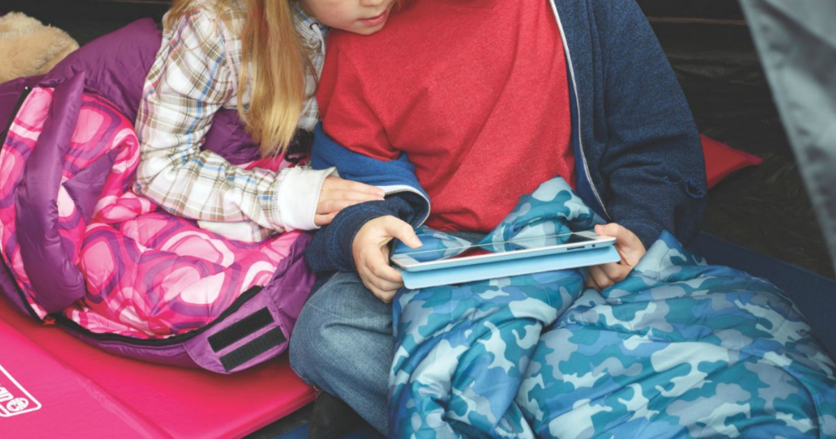 kids sitting in sleeping bags inside a tent looking at a tablet