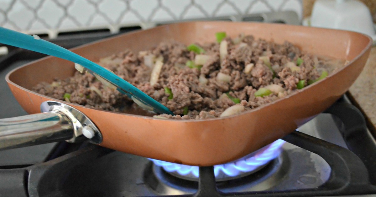 square copper pan over gas stove burner cooking meat and veggies