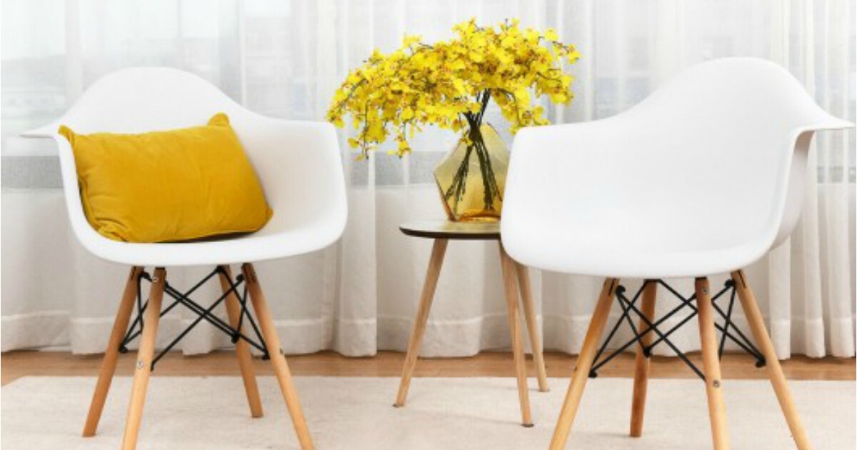 two white midcentury chairs with a yellow pillow arranged in front of curtains