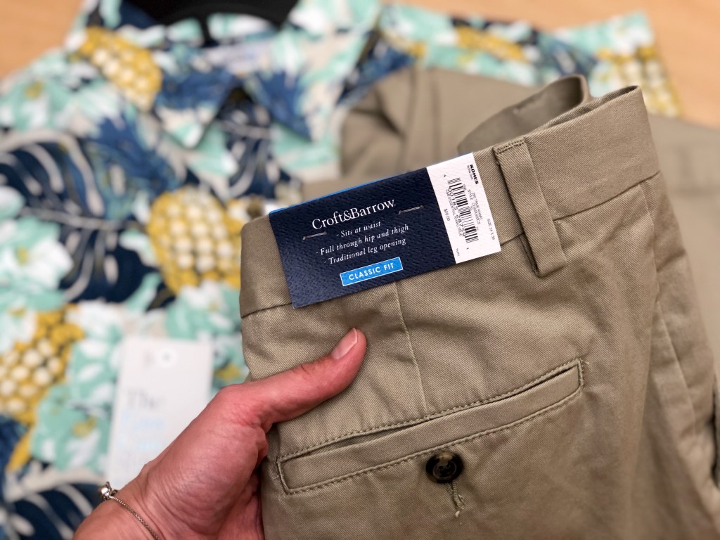 mens pants being held by a ladies hand with a Hawaiian print button up shirt laying behind it