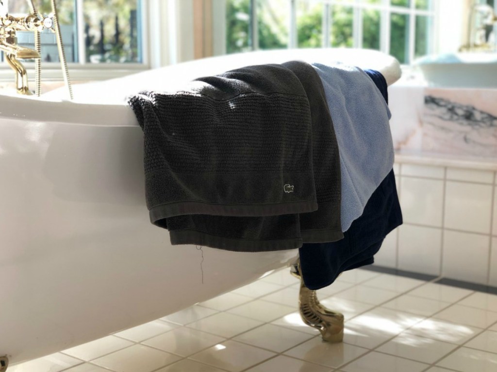 three Lacoste bath towels hanging over a vintage bath tub