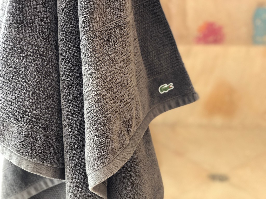 grey Lacoste bath towel hanging in a bathroom