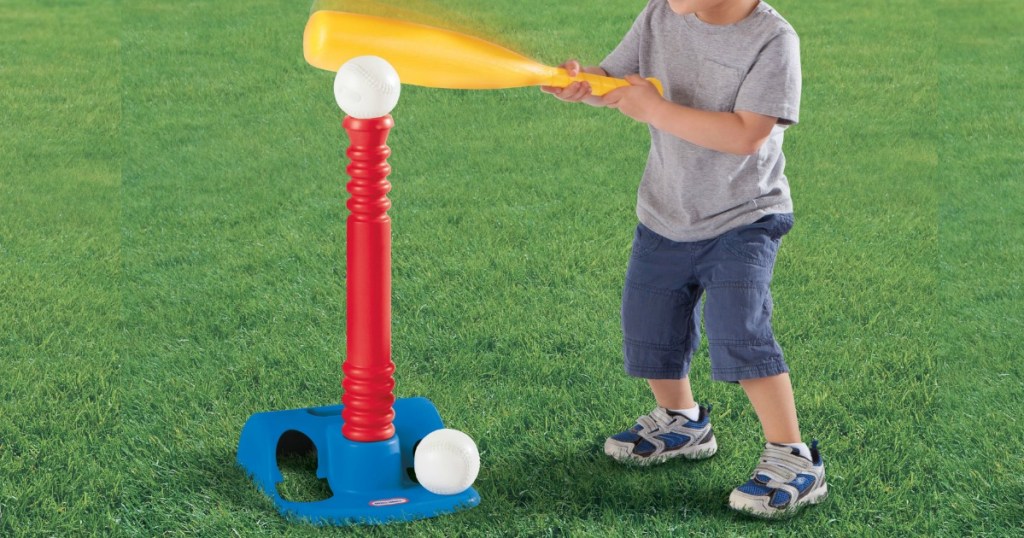 little kid hitting a ball off of a tee in the grass