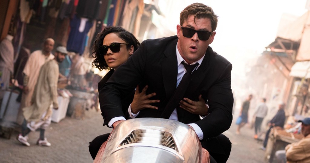 Chris Hemsworth and Tessa Thompson riding a motorcycle through a street market