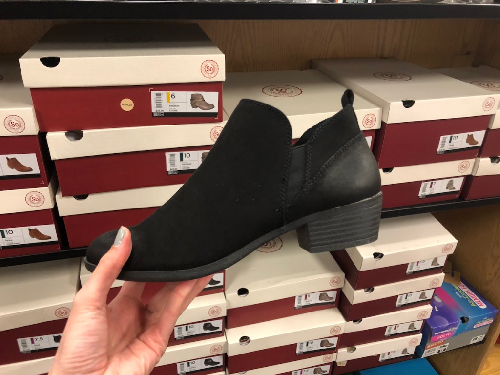 hand holding pair of black booties in front of shoes boxes