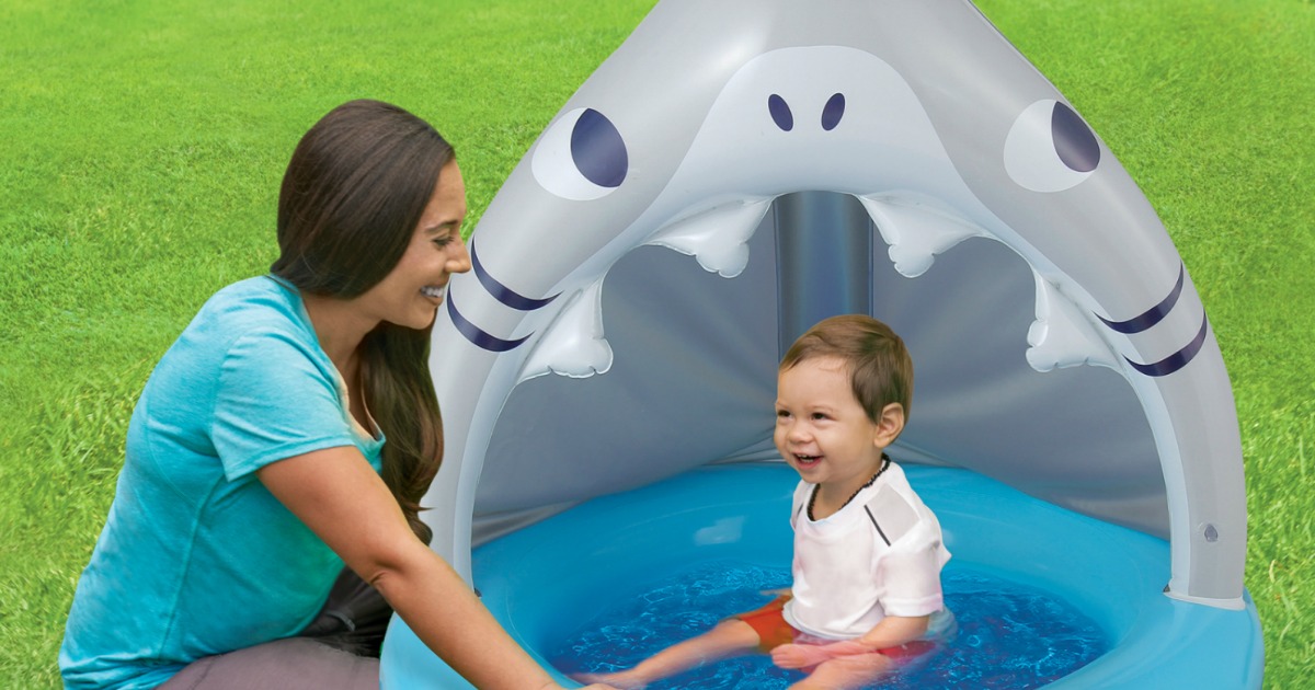 woman next to baby sitting in an inflatable shark-shaped pool