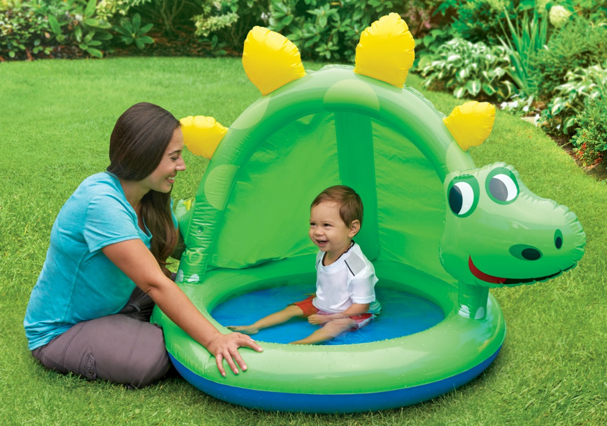 woman next to baby sitting in an inflatable dinosaur-shaped pool