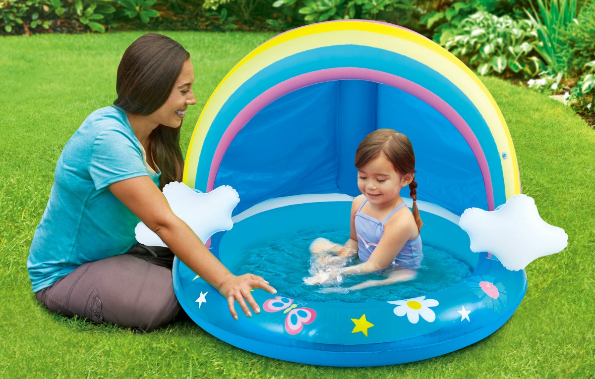 woman next to baby sitting in an inflatable rainbow-shaped pool