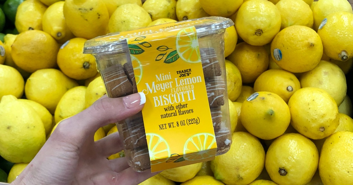 Woman holding container of Trader Joe's Mini Lemon Biscotti in front of lemon display in store