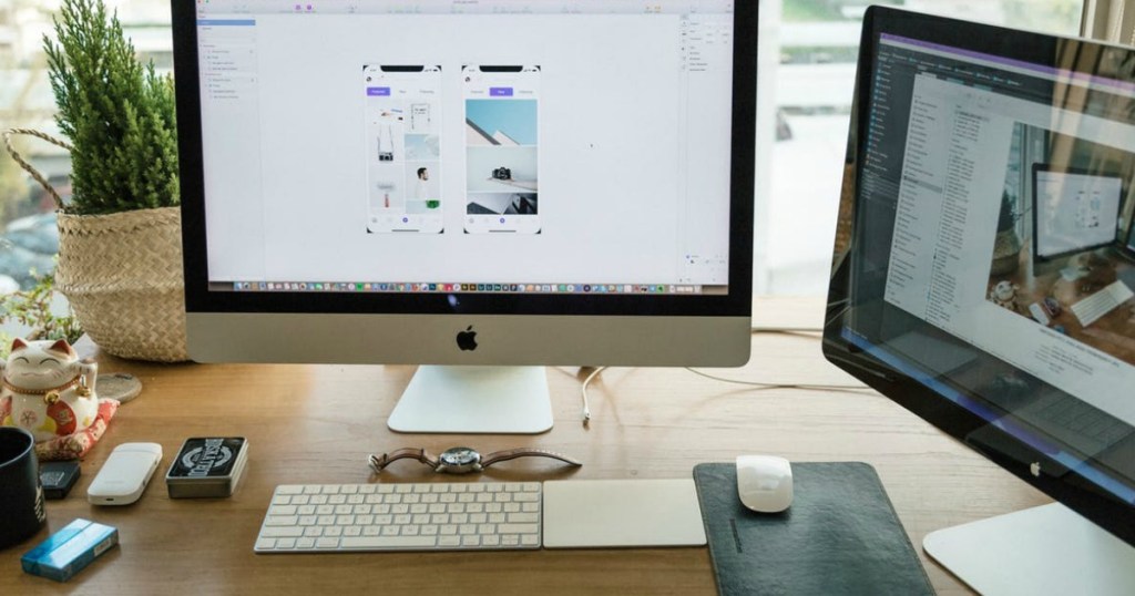 two apple onlineputers and magic apple keyboard sitting on desk with various items also on desk