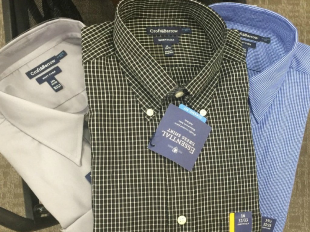 three men's dress shirts on a cart in a store