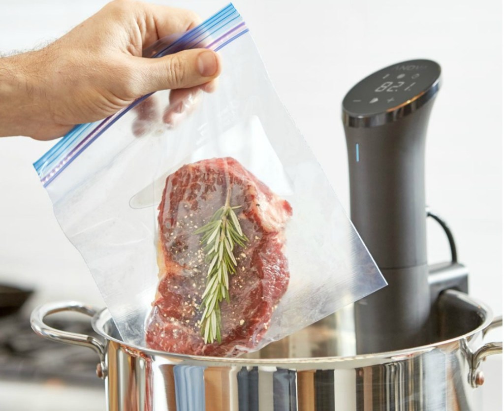 hand holding steak in zipped bag above pot with precision cooker in pot